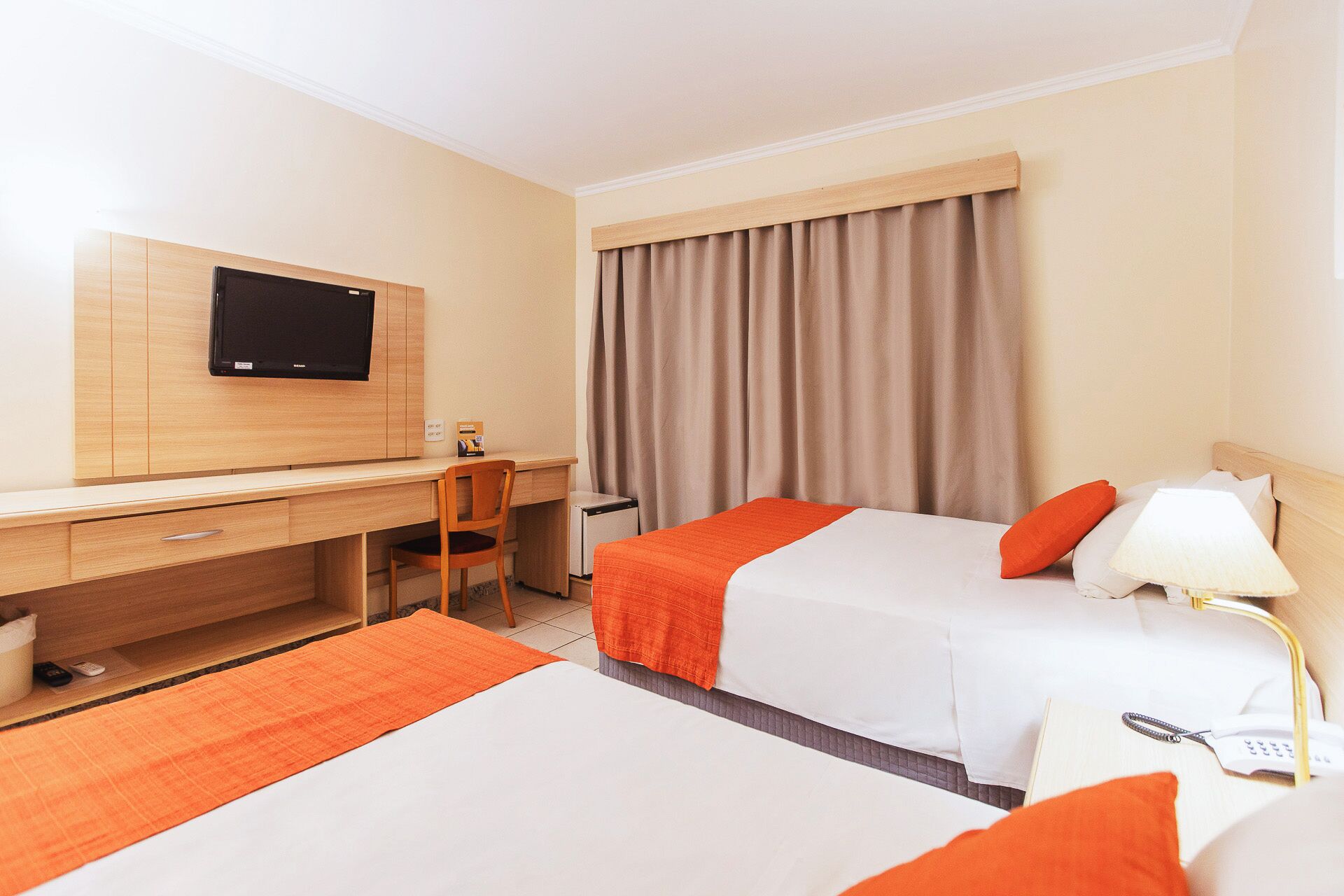 A hotel room with a desk, two beds, a TV, and curtains.