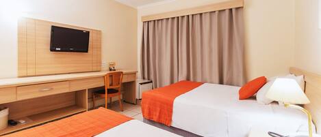 A hotel room with a desk, two beds, a TV, and curtains.