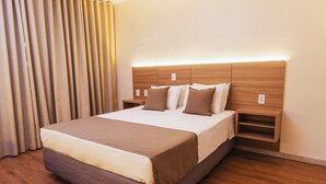 Una habitación de hotel con una cama grande, cabecera de madera, mesitas de noche y una cortina.
