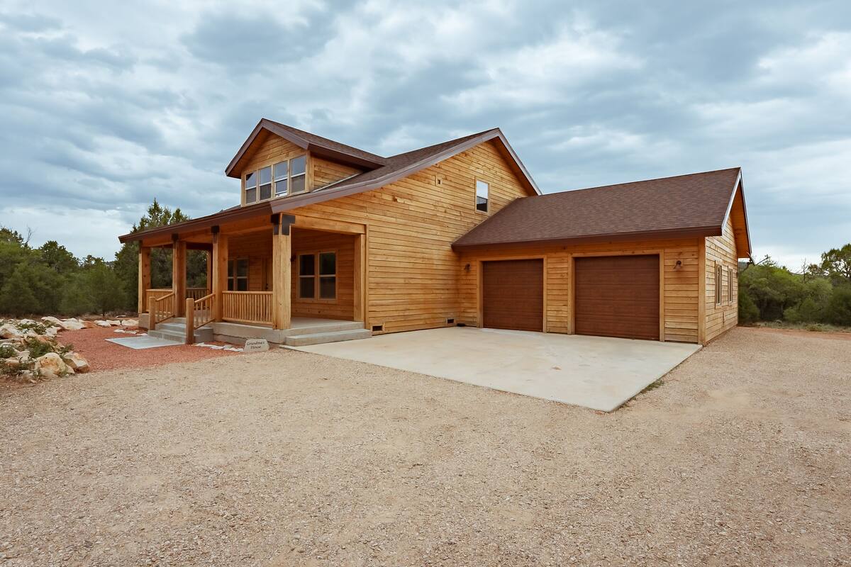 A two-story wooden house with a covered porch, a garage, and a gravel driveway.
