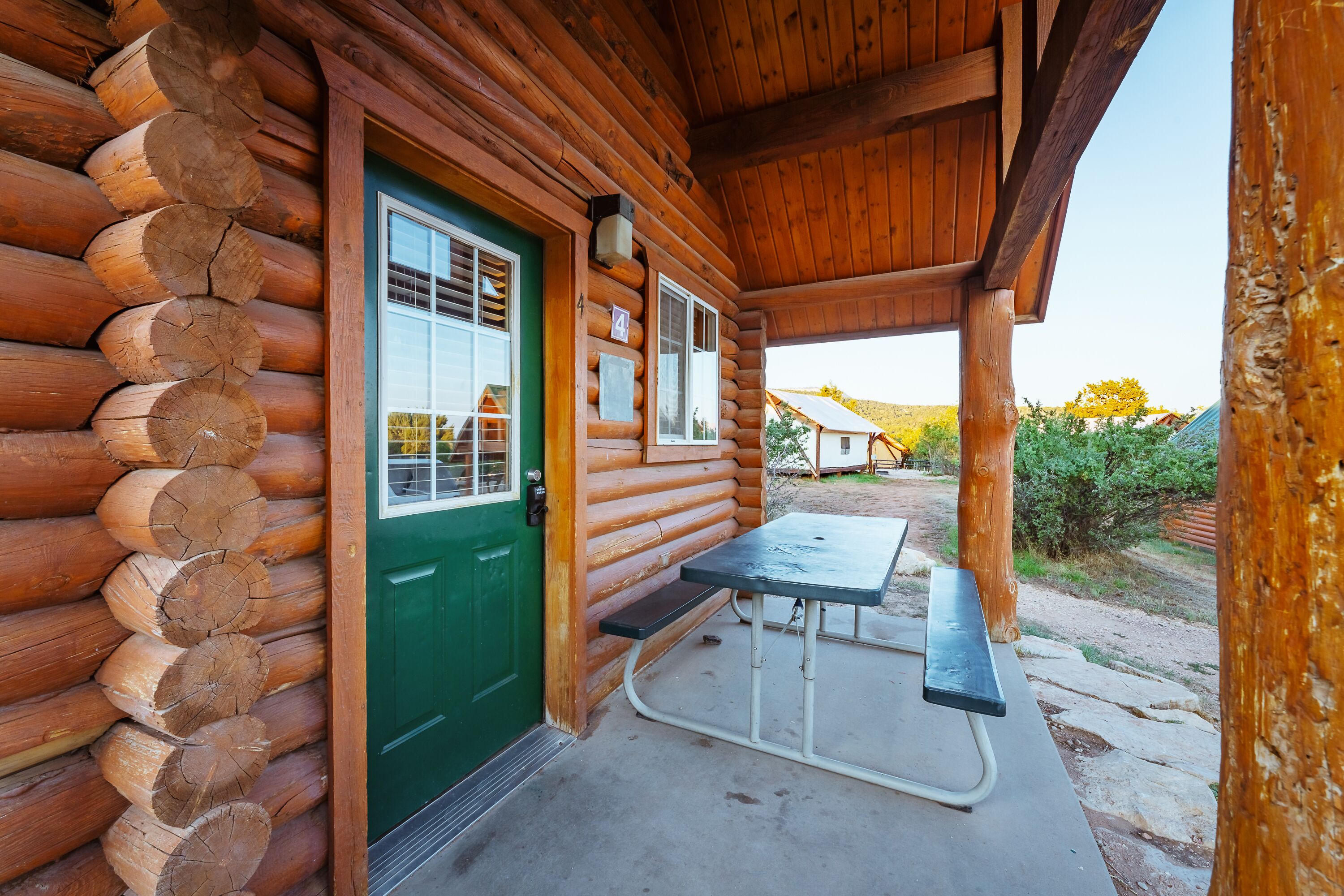 A log cabin with a green door, a covered porch, and a picnic table.