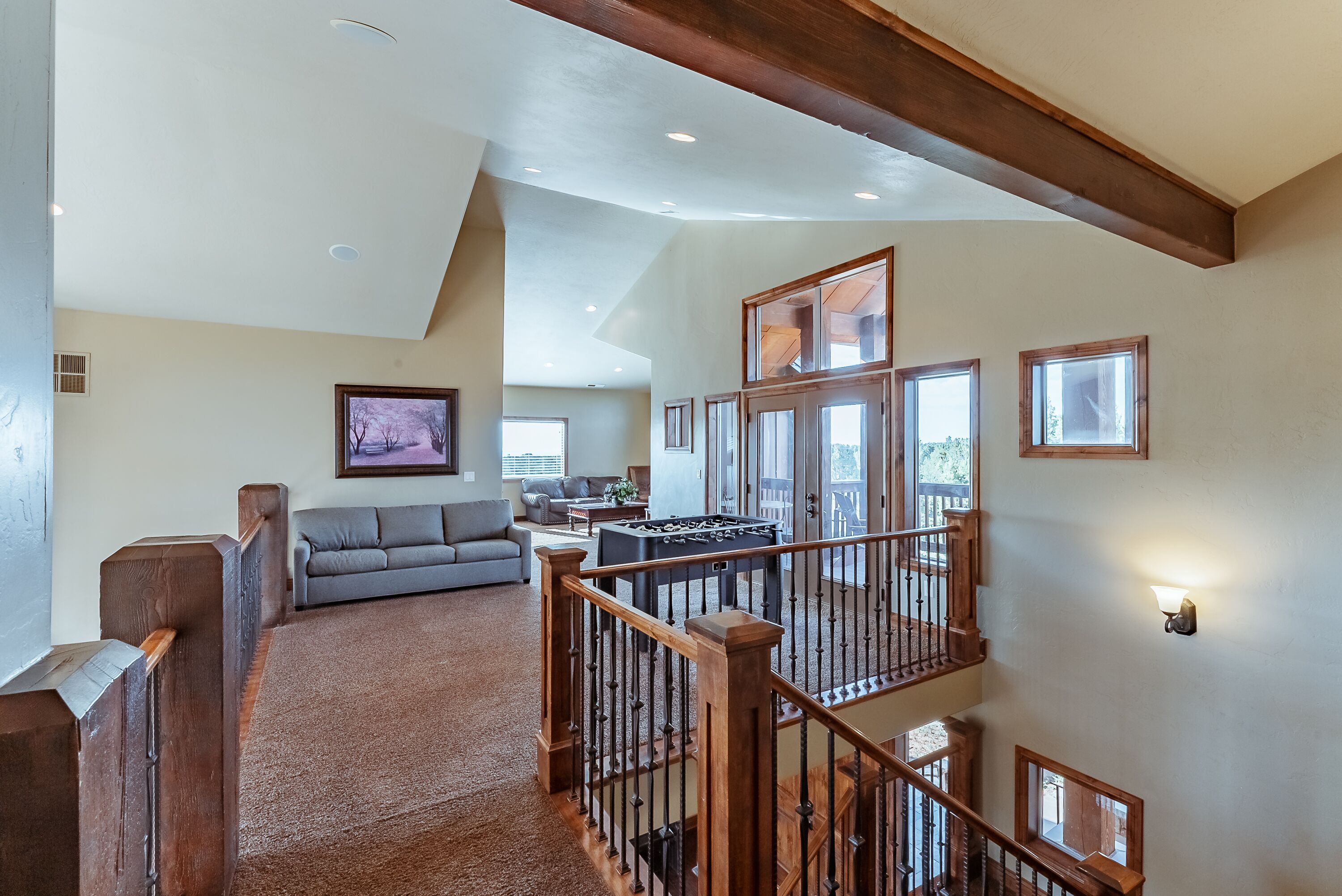 A spacious living area with a high ceiling, wooden beams, a staircase, and a large window.
