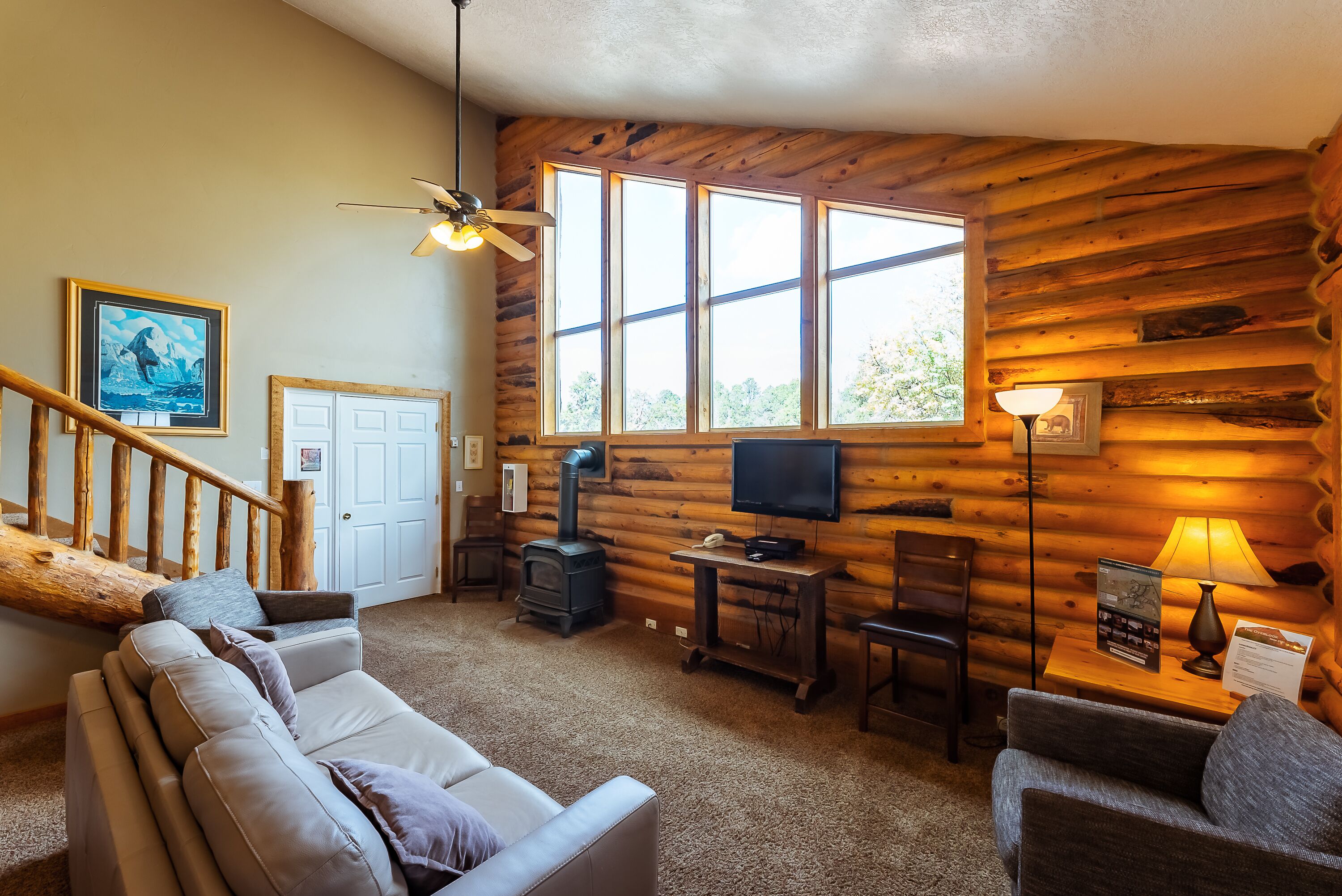 A log cabin interior with a sofa, a television, a fireplace, and a staircase.