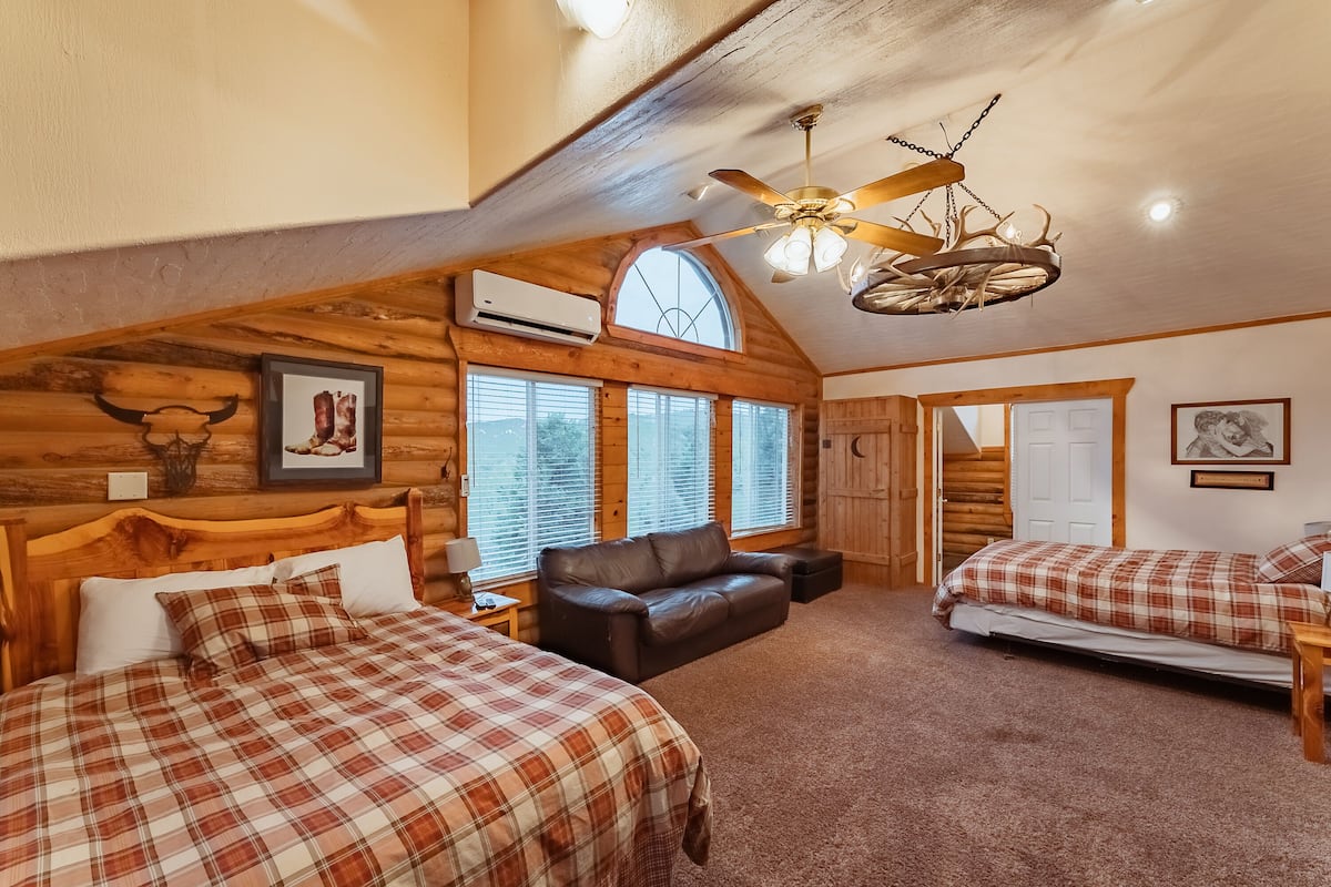 A log cabin bedroom with two beds, a leather sofa, and a ceiling fan.