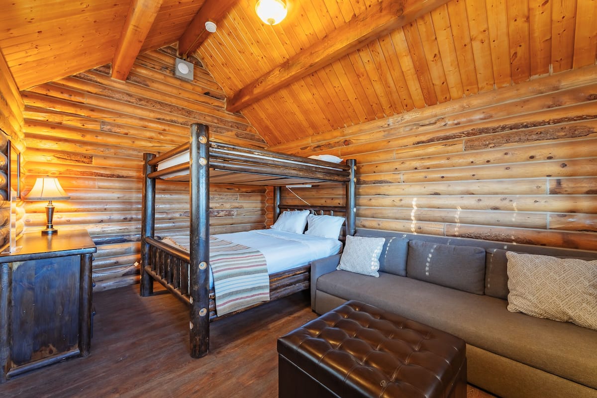 A log cabin bedroom with a bunk bed, a sofa, a table, and a lamp.