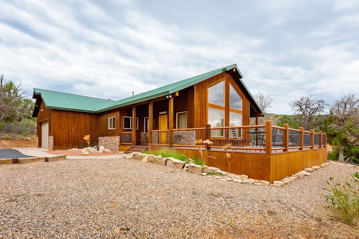A wooden cabin with a green roof, large windows, and a deck.