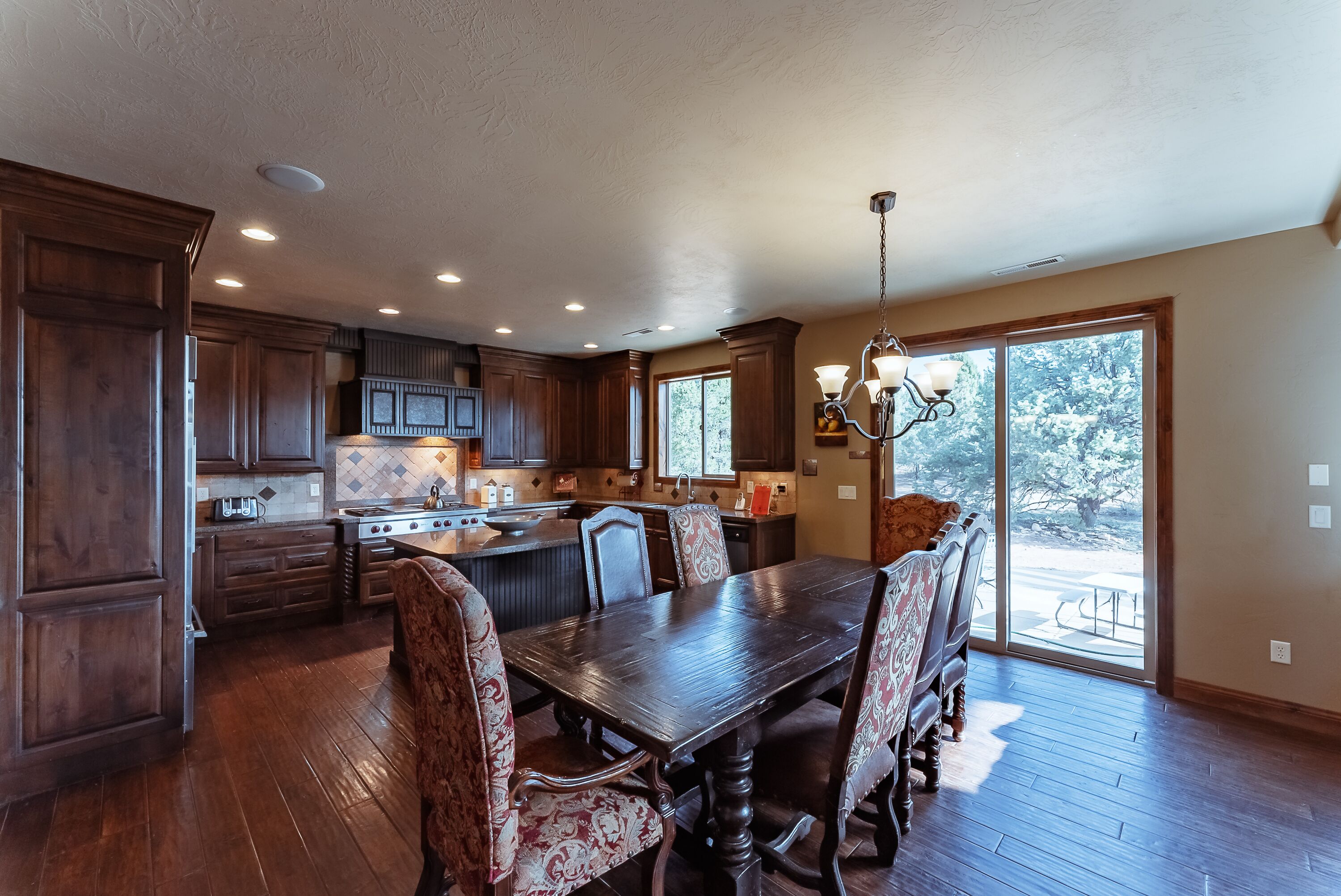 A spacious kitchen with wooden cabinets, a dining table with chairs, and a large window providing a view of the outdoors.