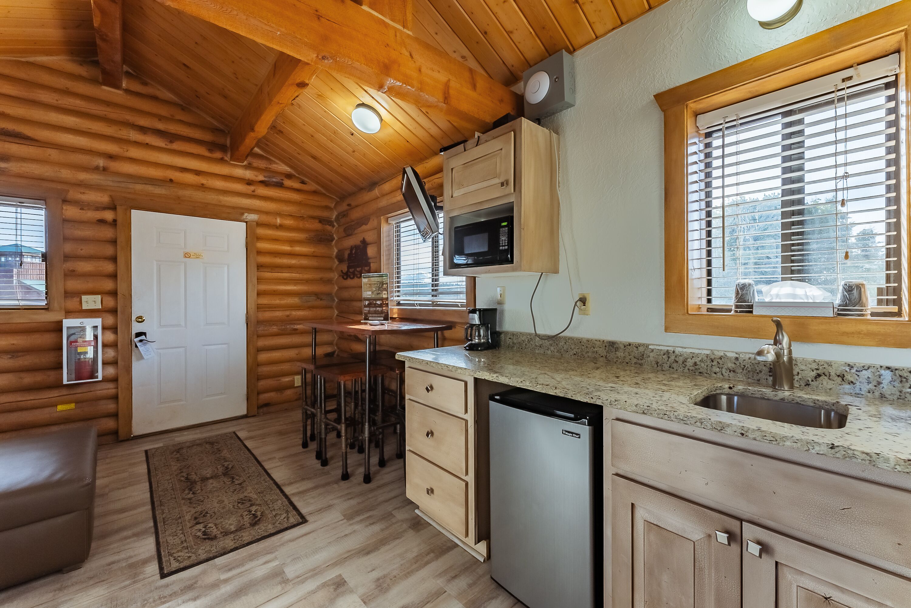 A log cabin with a kitchen area featuring a microwave, sink, and wooden cabinets.