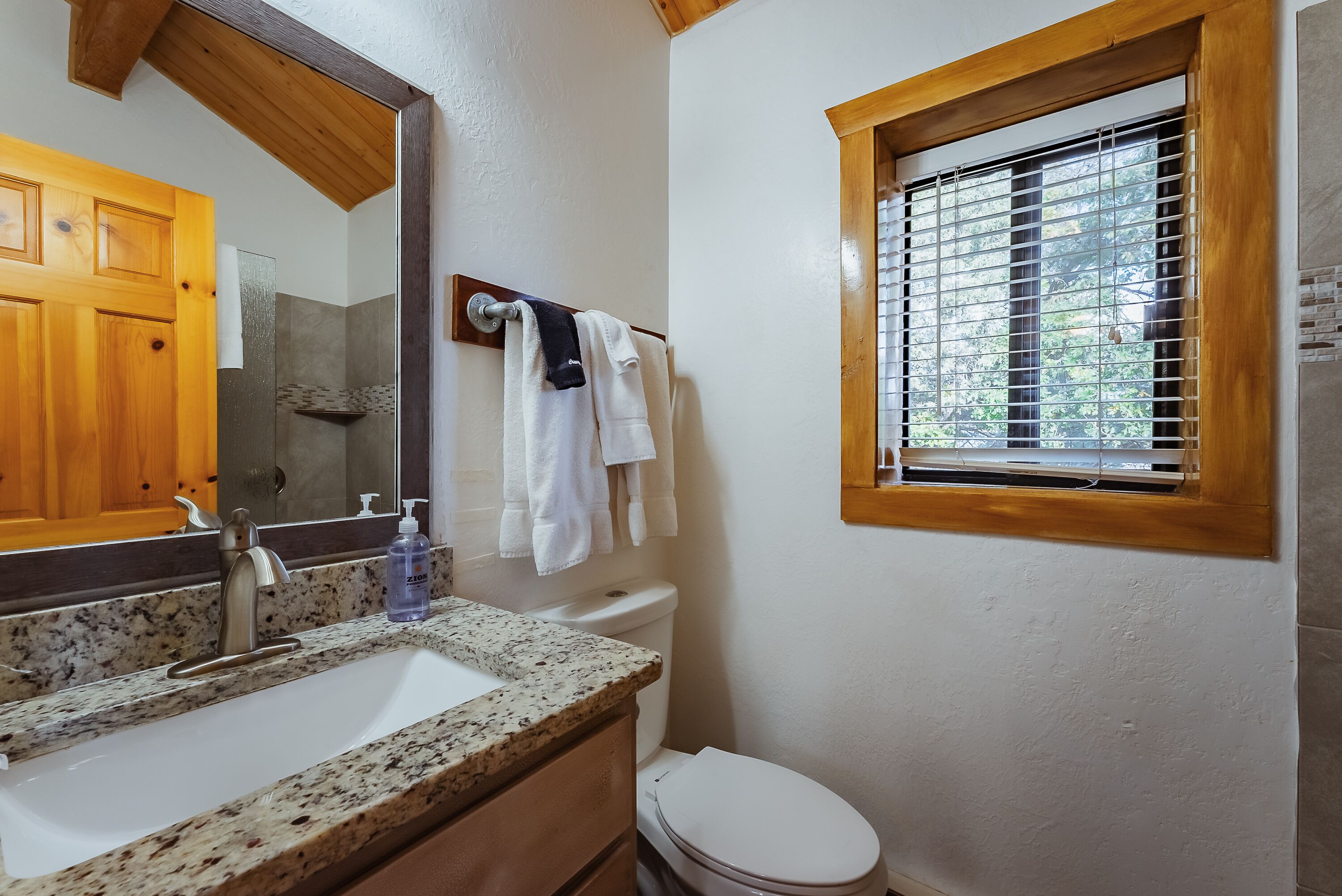 A bathroom with a granite countertop sink, a wooden door, a window with blinds, and a towel rack with towels.