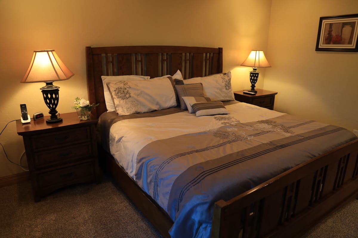 A neatly made bed with a wooden headboard, two bedside tables with lamps, and a framed picture on the wall.