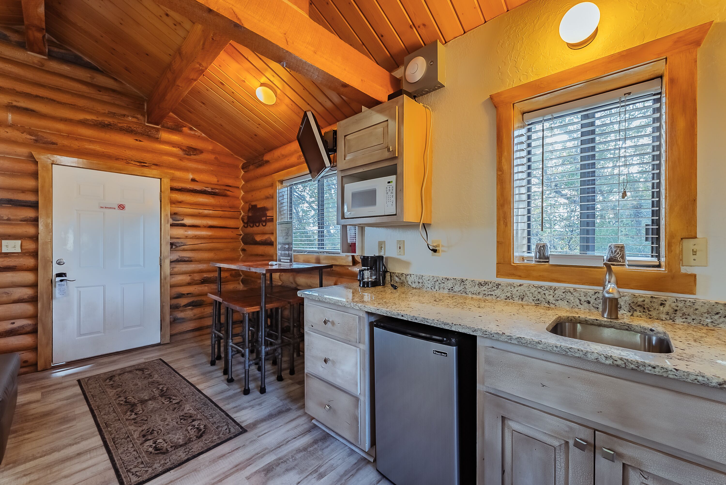 A log cabin interior with a kitchen area featuring a sink, microwave, and bar stools.