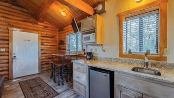 A log cabin interior with a kitchen area featuring a sink, microwave, and bar stools.