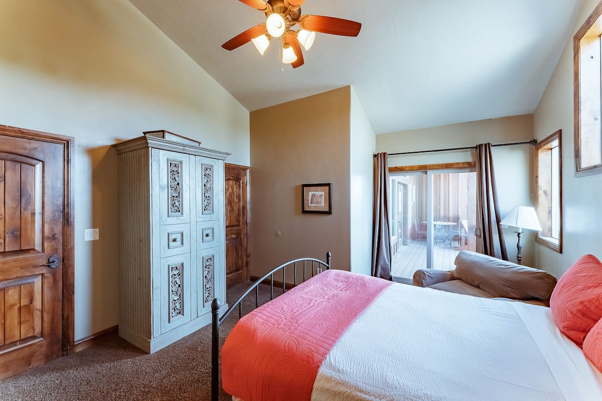 A bedroom with a bed, a ceiling fan, a wardrobe, and a view of the outdoors.