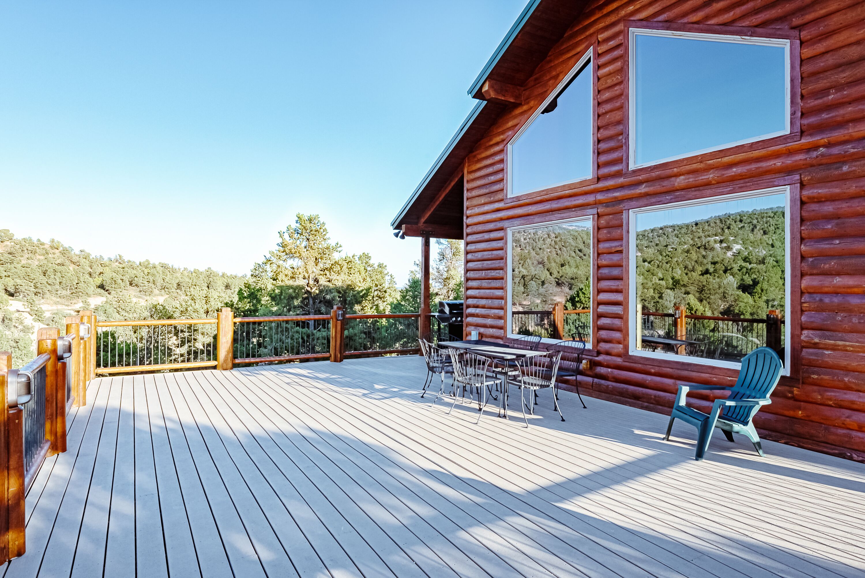 A wooden deck with a dining area, large windows, and a view of a forested hillside.