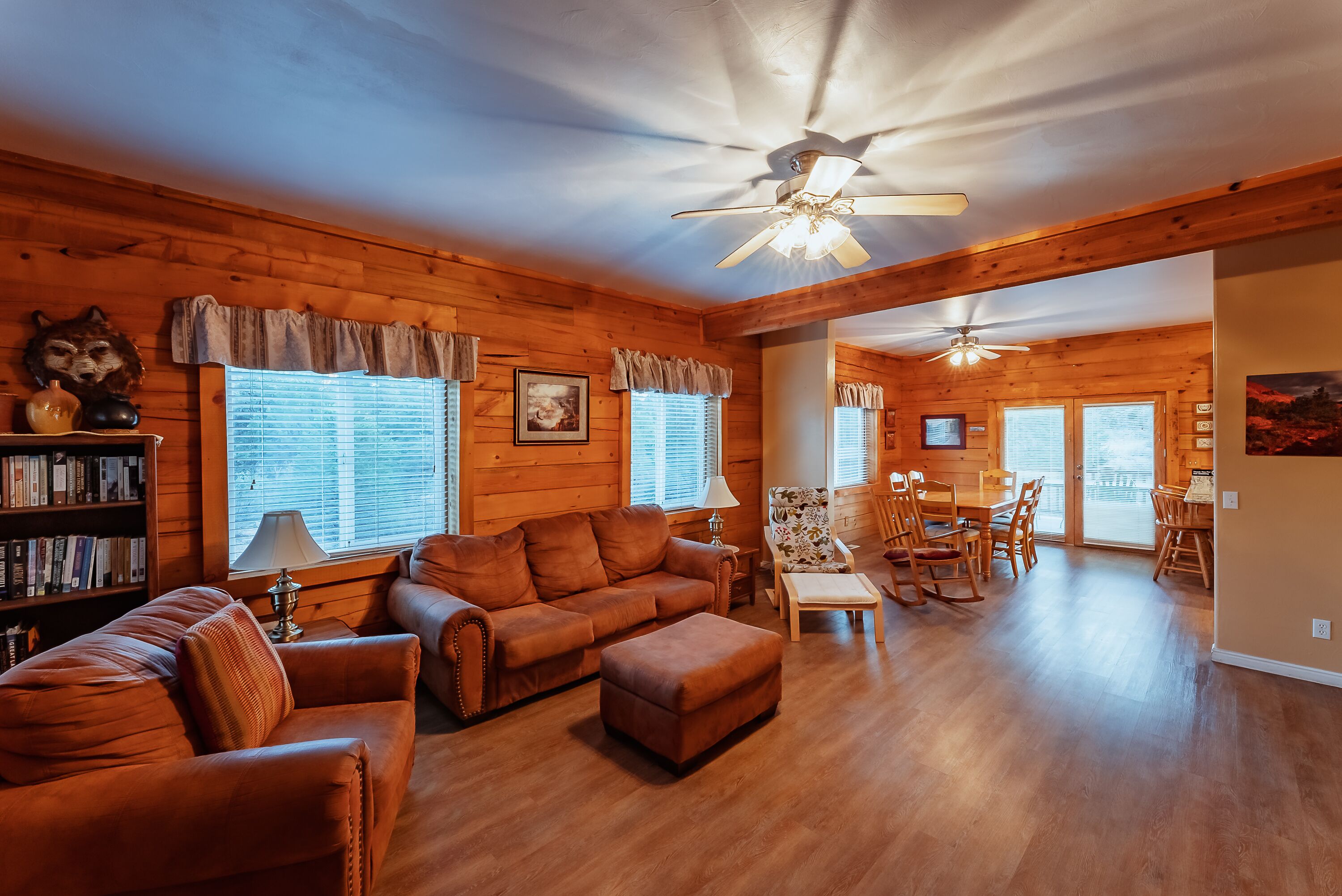 A cozy log cabin interior with a living room, dining area, and a ceiling fan.
