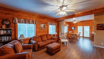 A cozy log cabin interior with a living room, dining area, and a ceiling fan.