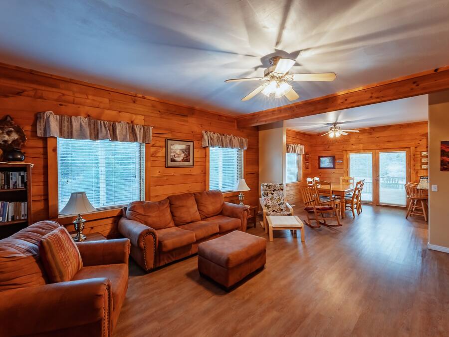 A cozy log cabin interior with a living room, dining area, and a ceiling fan.