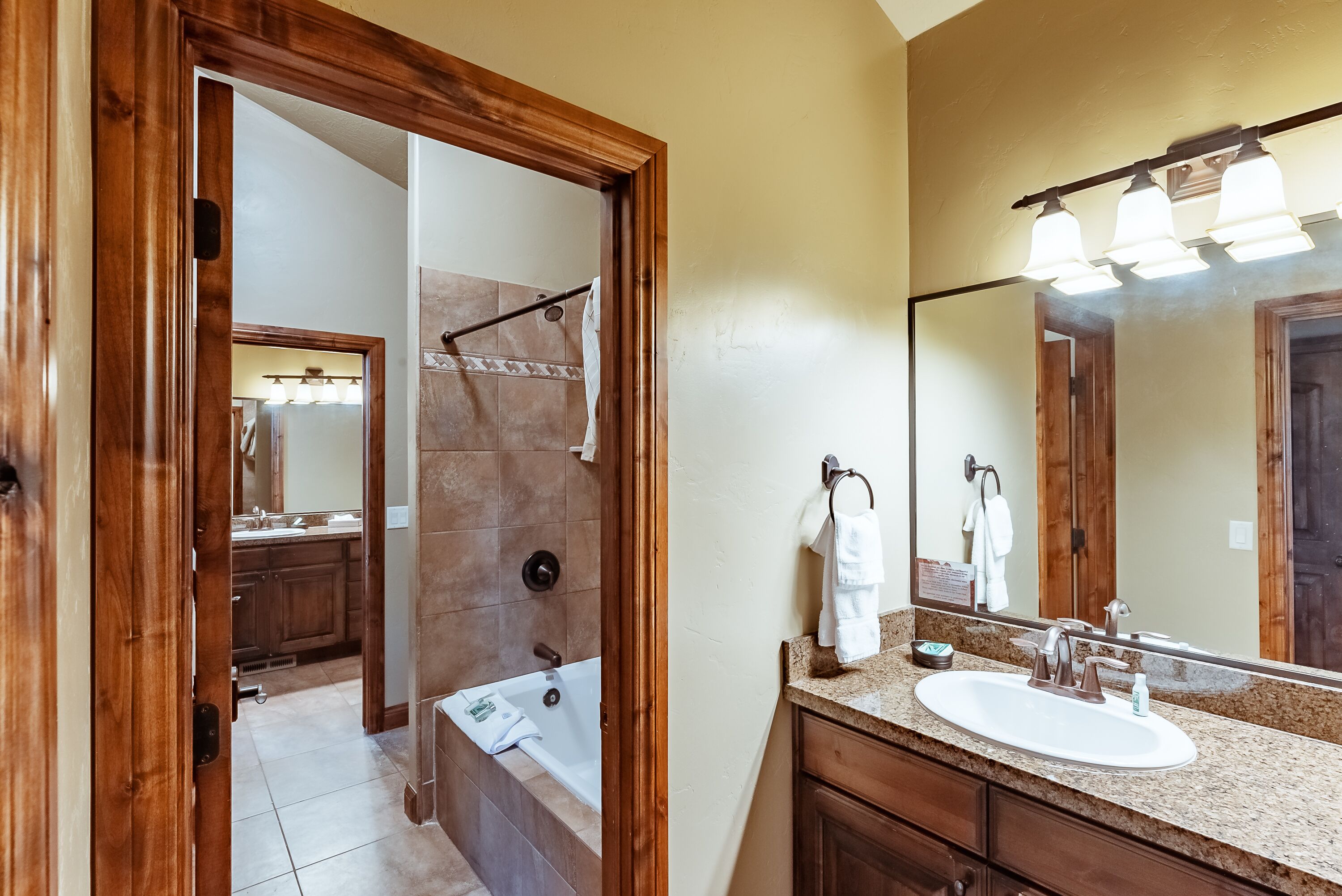 A bathroom with a wooden door, a sink, a mirror, and a shower area.