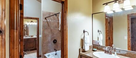 Un baño con puerta de madera, lavamanos, espejo y zona de ducha.