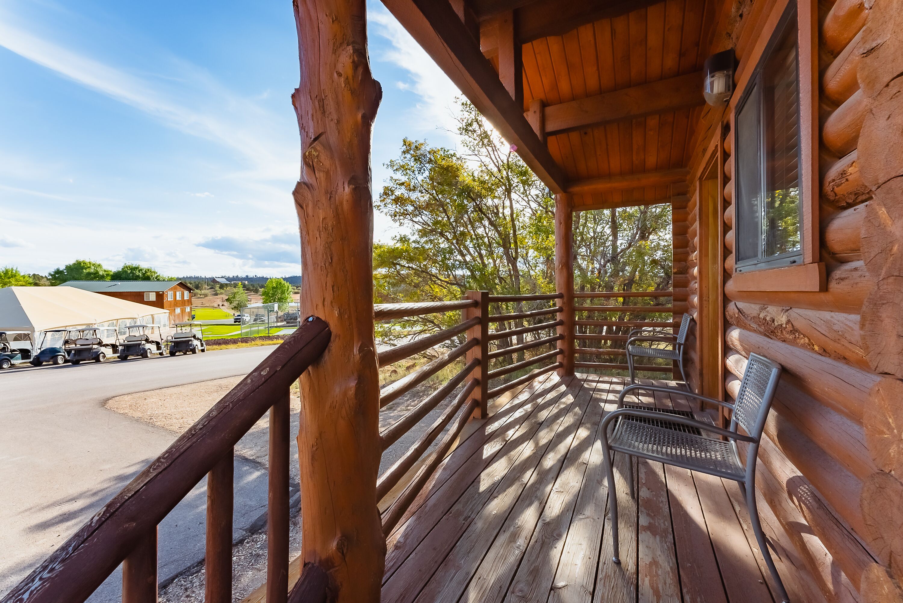 A wooden cabin with a porch, a view of a parking lot, and a distant building.