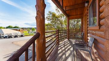 A wooden cabin with a porch, a view of a parking lot, and a distant building.