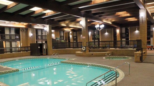 An indoor swimming pool with multiple lanes, a lifeguard station, and a seating area with a view of the pool. - Ramada by Wyndham Alpena (Alpena)