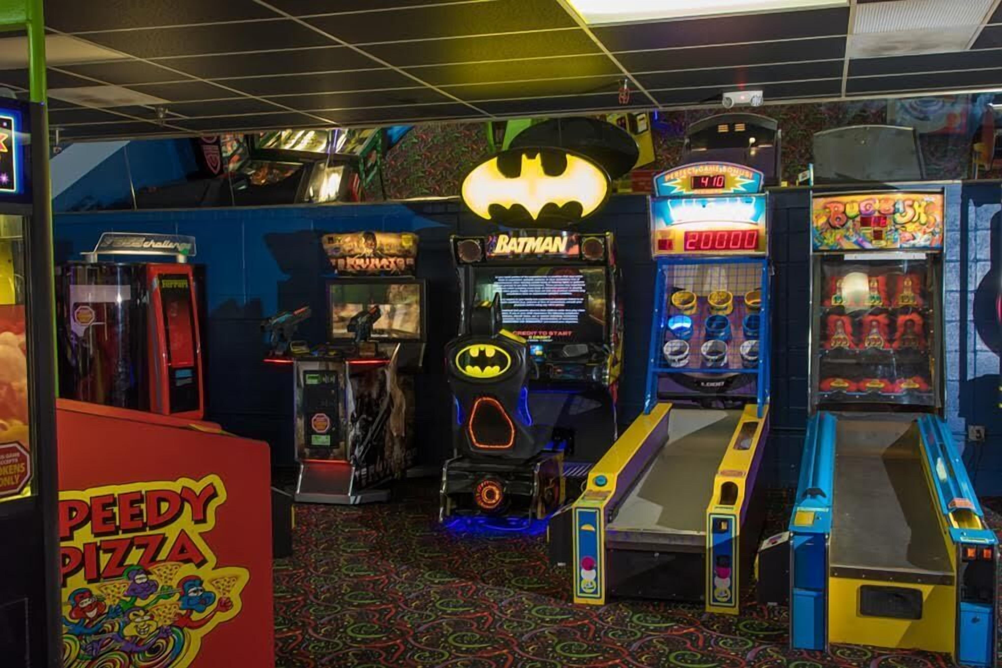 Una habitación con juegos de arcade, incluyendo Batman, Buzz Lightyear y un juego de Speedy Pizza.