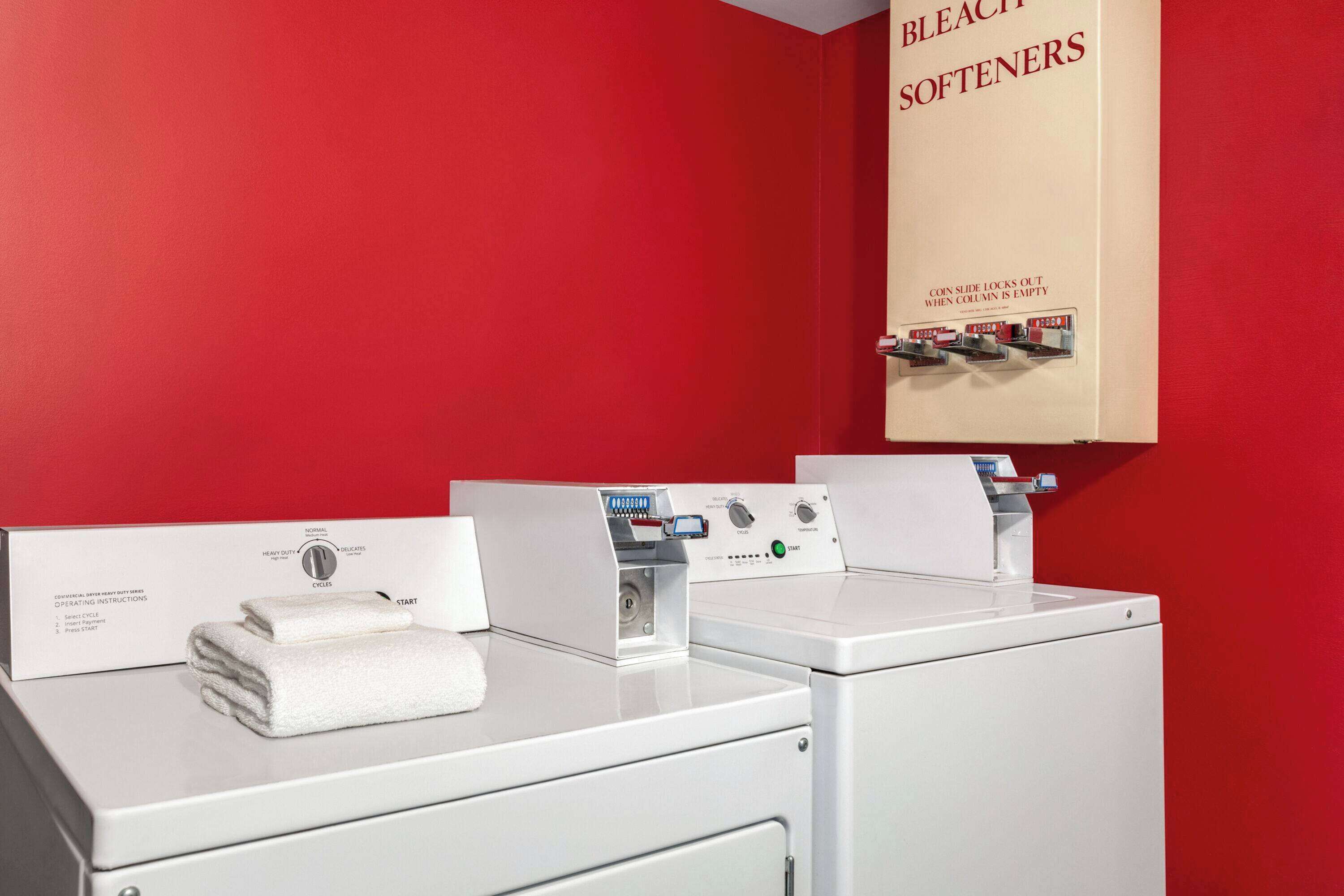 Une buanderie équipée de trois machines à laver et dotée d’un mur rouge.