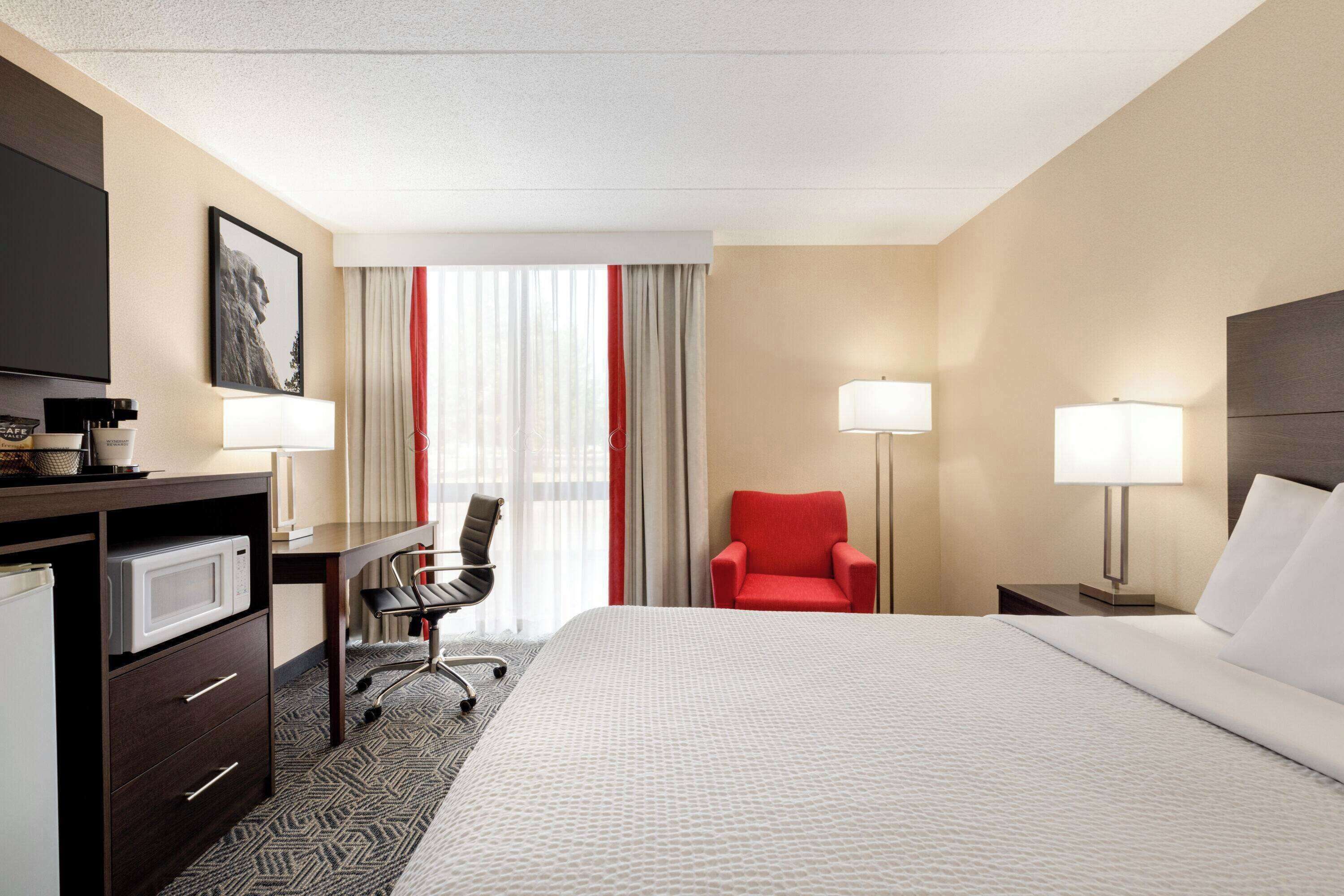 A hotel room with a bed, desk, chair, TV, and lamps.