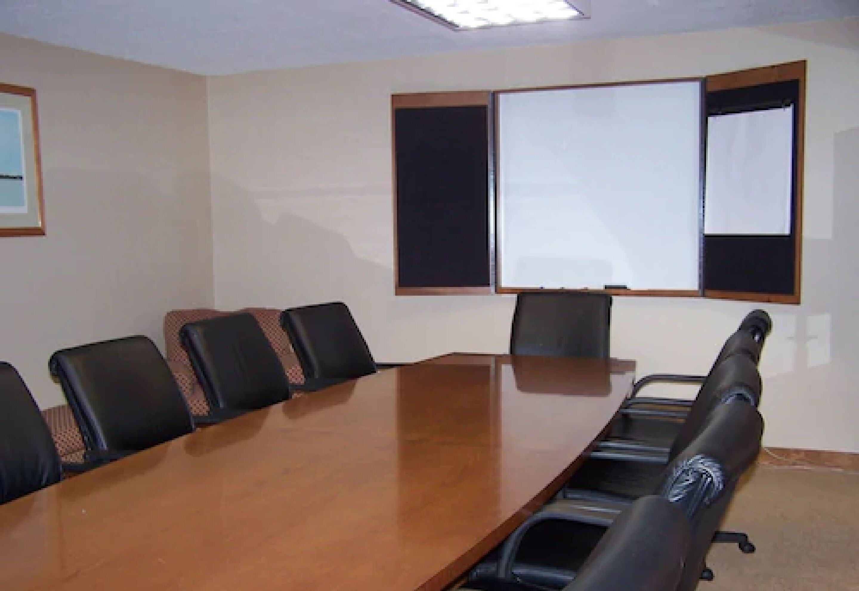 A conference room with a long table, six chairs, and two projection screens.