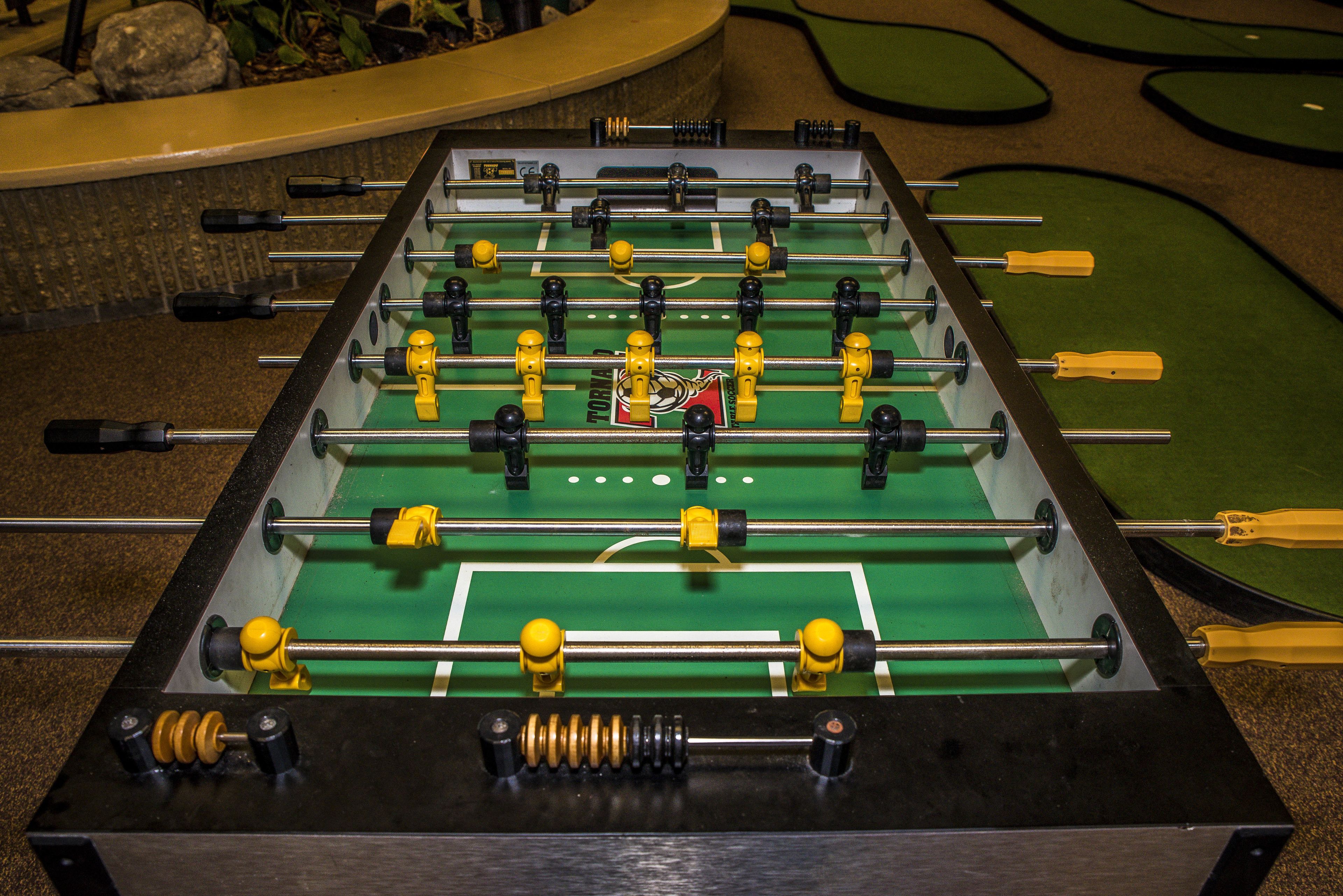 Ein Kicker mit grüner Spielfläche und gelben und schwarzen Spielfiguren.
