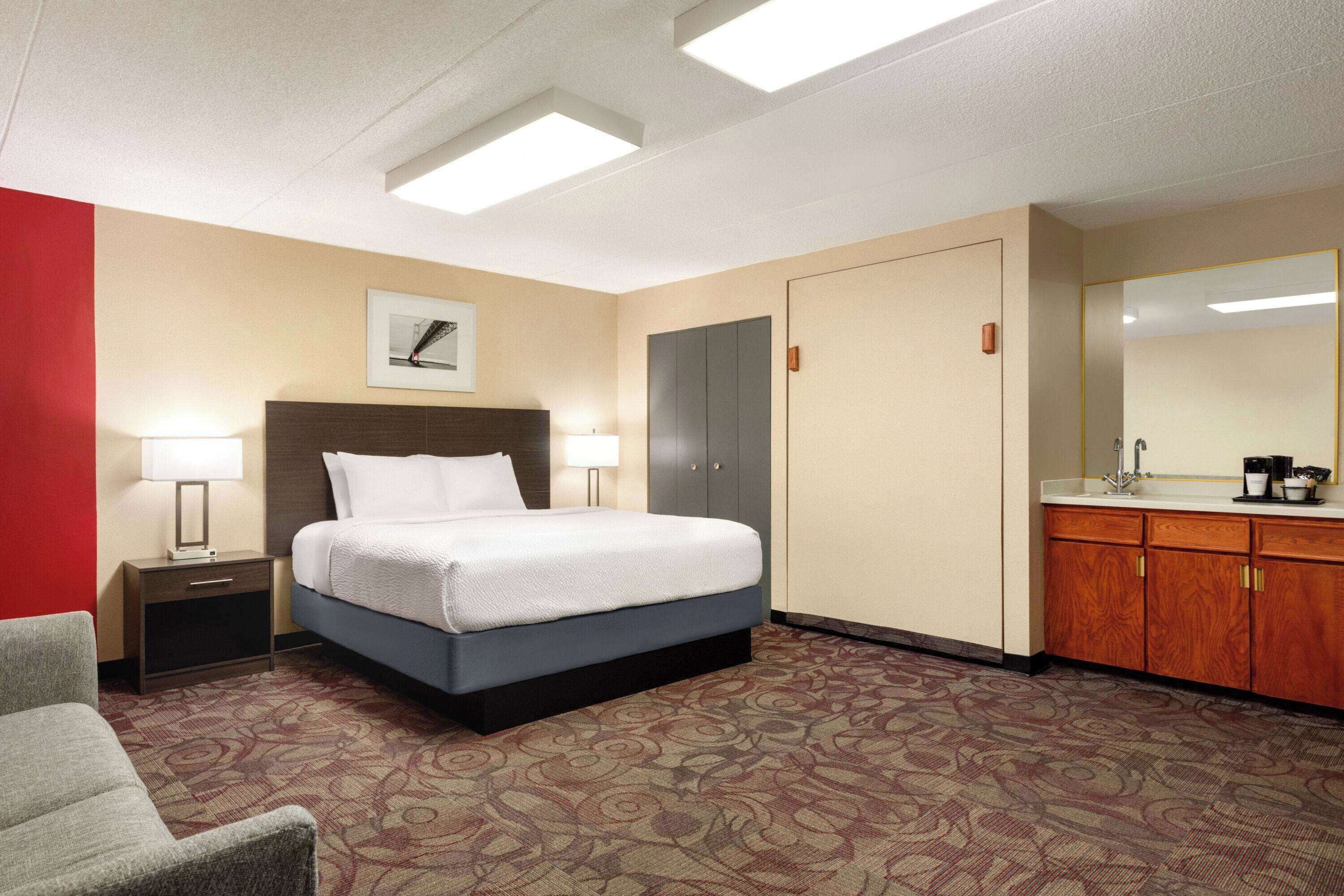 A hotel room with a bed, a nightstand with a lamp, a dresser, and a mirror.