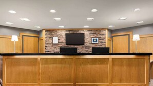 A reception area with a wooden counter, a stone accent wall, a flat-screen TV, and framed awards. - Ramada by Wyndham Alpena (Alpena)