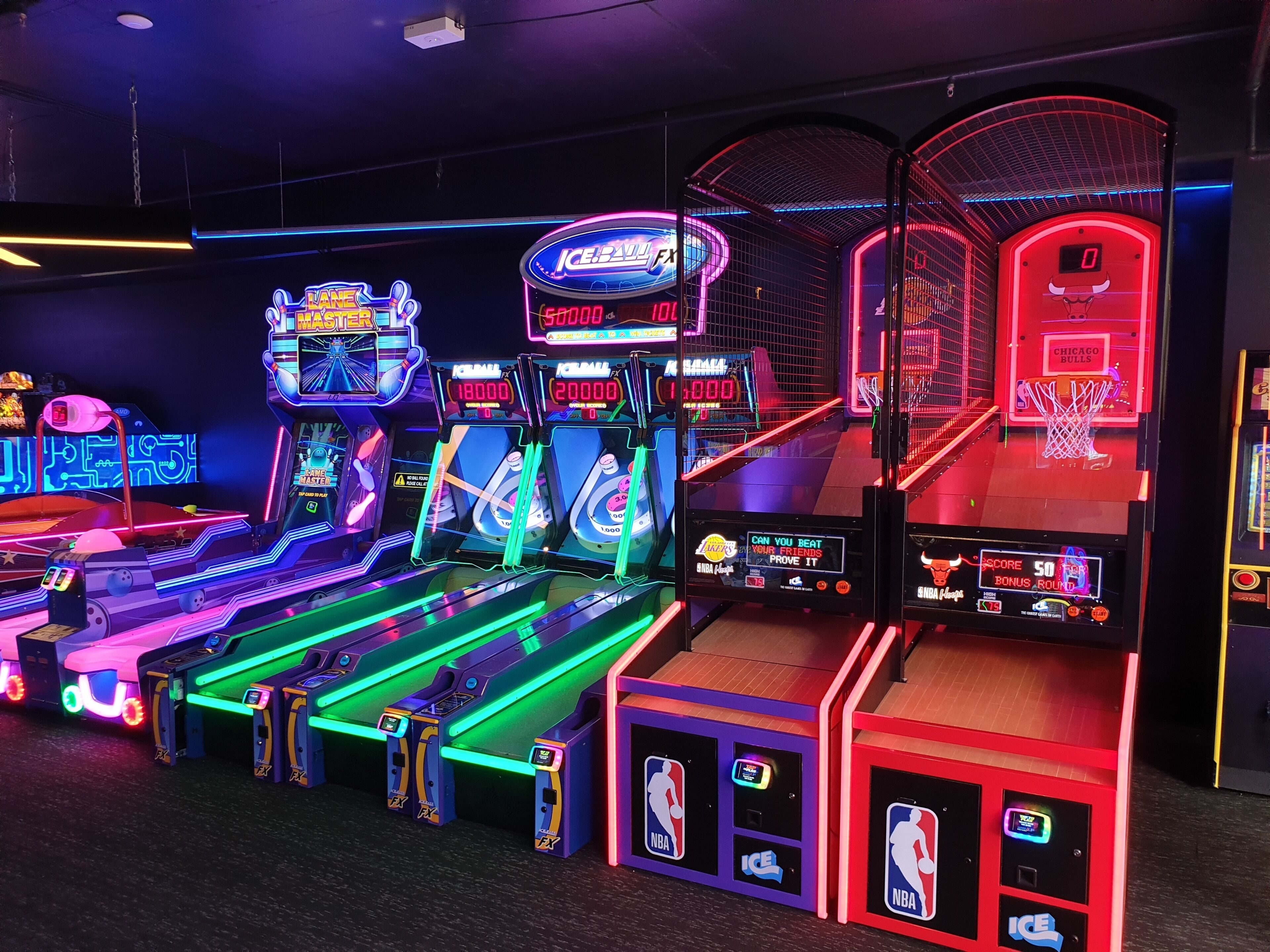 Una hilera de máquinas de baloncesto recreativas con luces de neón y pantallas de puntuación digital.