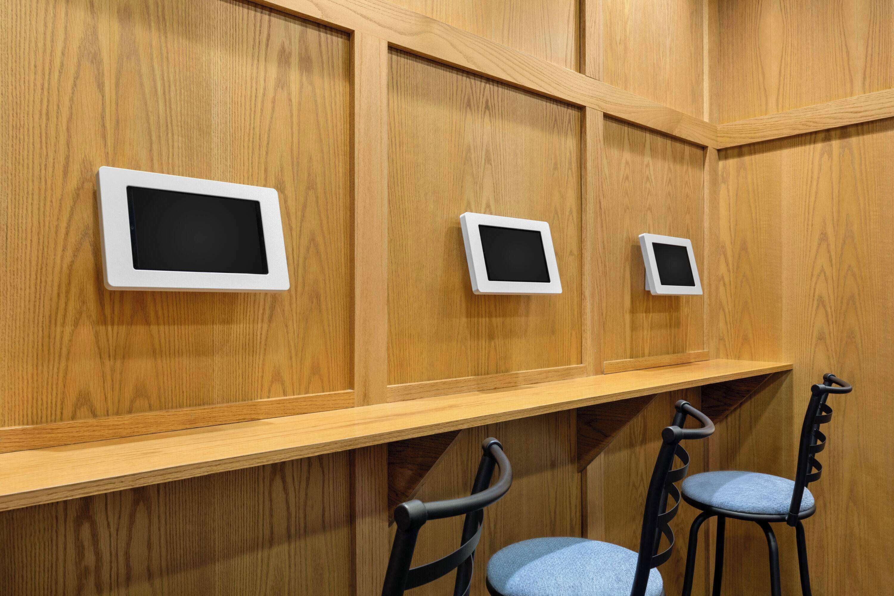 Una habitación con paneles de madera, tres monitores montados en la pared y dos sillas negras con cojines azules.