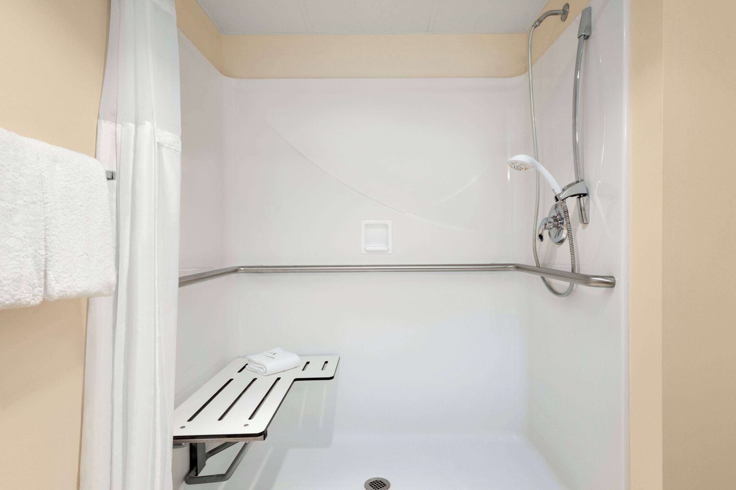 A small, enclosed shower area with a white showerhead, a handheld shower attachment, and a grab bar for support.