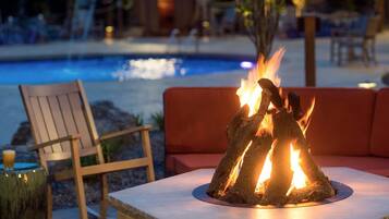 Un área junto a la piscina con una chimenea, una silla de madera y un sofá rojo.