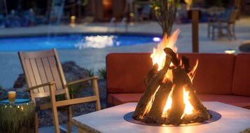 Un área junto a la piscina con una chimenea, una silla de madera y un sofá rojo.