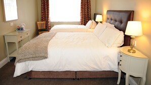 Habitación de hotel con dos camas, una mesita de noche con lámpara, una silla y un ventanal con cortinas.