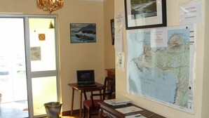 Una habitación con suelo de madera, un escritorio con papeles, una computadora portátil, un mapa en la pared y una puerta que da al exterior.