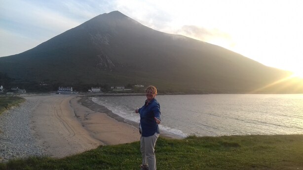Una persona de pie en la playa, con una montaña al fondo.