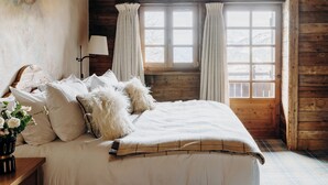 Una camera da letto accogliente in legno con un letto, cuscini, una lampada e una finestra con tende.