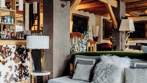 Una camera accogliente con divano, lampada, angolo bar con bottiglie e soffitto in legno rustico.