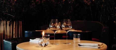 Une table ronde en bois, avec deux verres à vin, un petit verre d’eau et une bougie allumée.