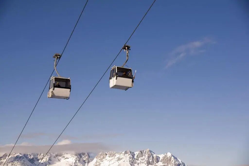 Deux téléphériques suspendus à des câbles, avec un ciel bleu en arrière-plan.