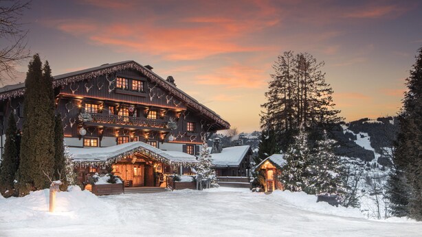 Un'ampia baita a più piani in legno, con l'ingresso innevato e luci festive.