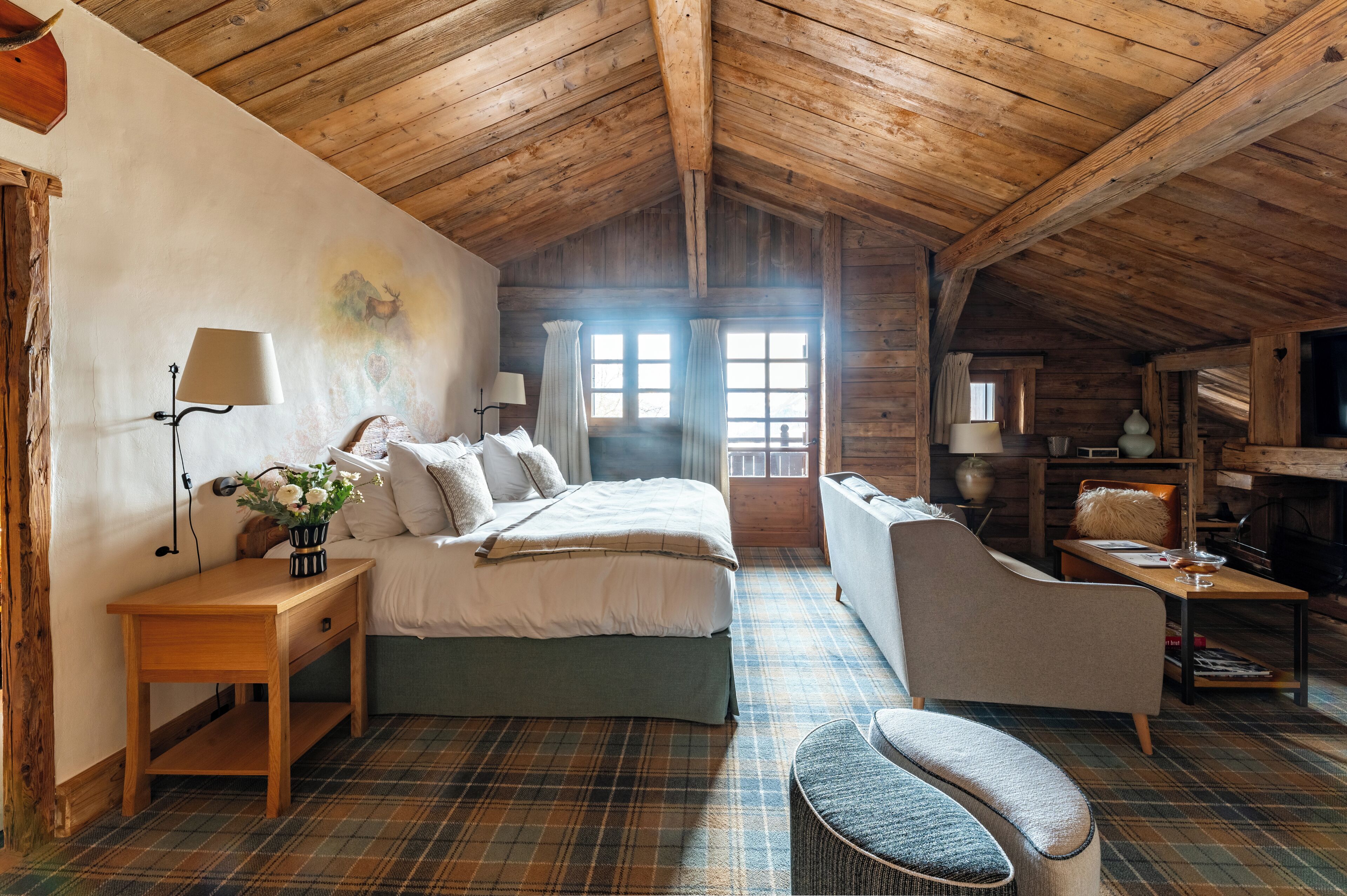 Un dormitorio acogedor y rústico con techo de madera, una cama grande, un sofá y una mesita de noche con una lámpara.