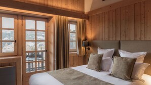 A wooden-paneled bedroom with a large bed, a nightstand, and a window with curtains. - La Ferme du Golf (Megeve)