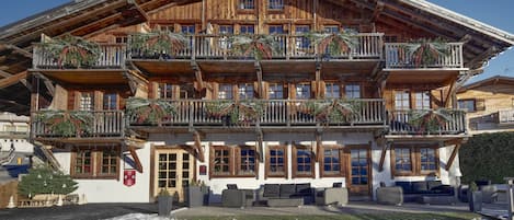 A wooden chalet with multiple balconies, outdoor seating, and a snow-covered ground.