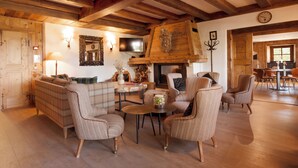 A cozy living room with a fireplace, wooden beams, a plaid sofa, and wicker chairs. - La Ferme du Golf (Megeve)